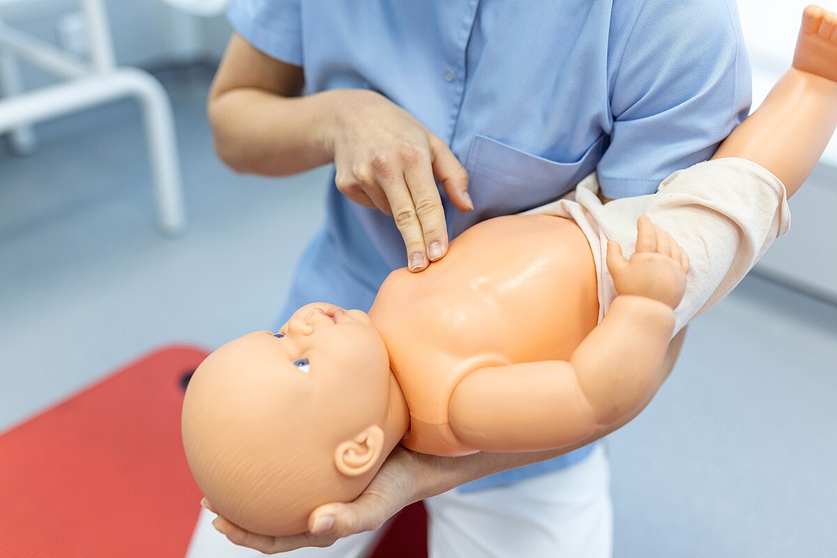 Frau hält Babypuppe und zeigt Reanimation