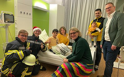 Feuerwehrfan Anas Bablis (Mitte) freute sich gemeinsam mit seinen Eltern über den Besuch der Flammen Freunde, Oberbügermeisterin Eva Weber (3.v.r.) und Sebastian Stief, Geschäftsführer des Josefinum (r.). Foto: KJF Augsburg / Pia Reiser